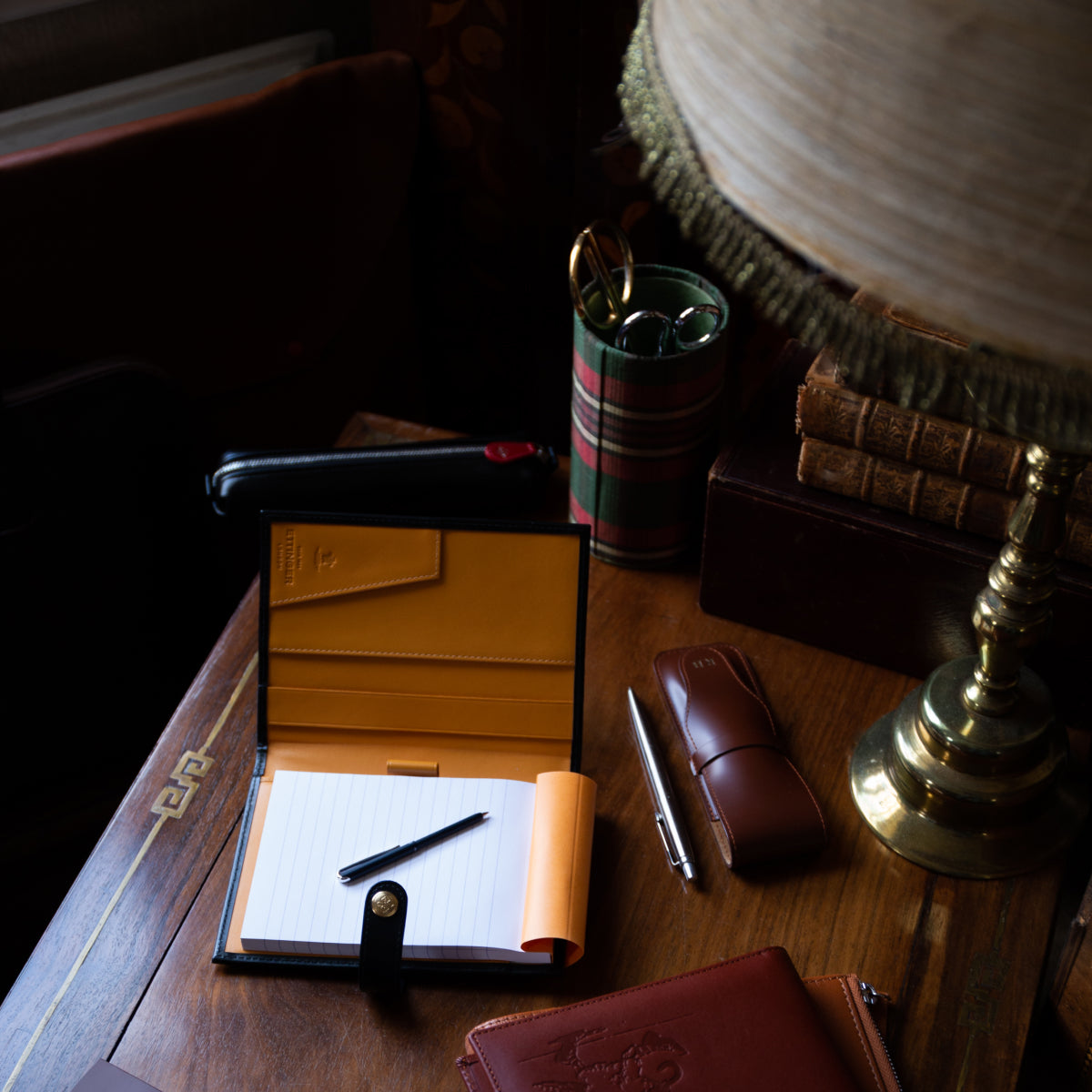 Open notepad with a pen, a pen case and other accessories on a wooden table